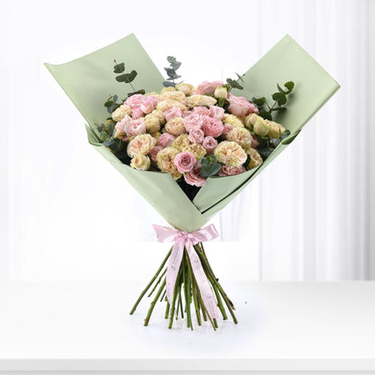 Pastel pink and cream roses wrapped in sage green paper with pink ribbon.
