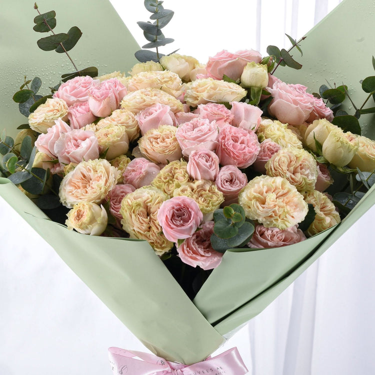 Soft pink and cream roses wrapped in sage green paper with delicate eucalyptus accents.