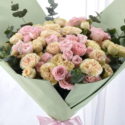 Pastel pink and cream roses wrapped in soft green paper with eucalyptus.