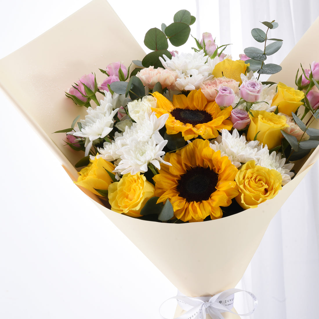 Vibrant sunflowers, yellow roses, white chrysanthemums, pink blooms, eucalyptus in cream wrap with white ribbon.