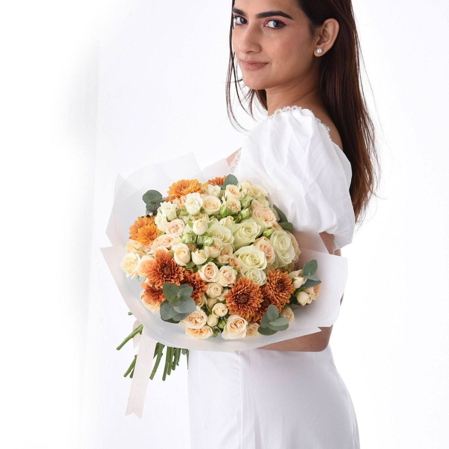Woman in white dress holds vibrant orange and cream floral bouquet against clean white background.