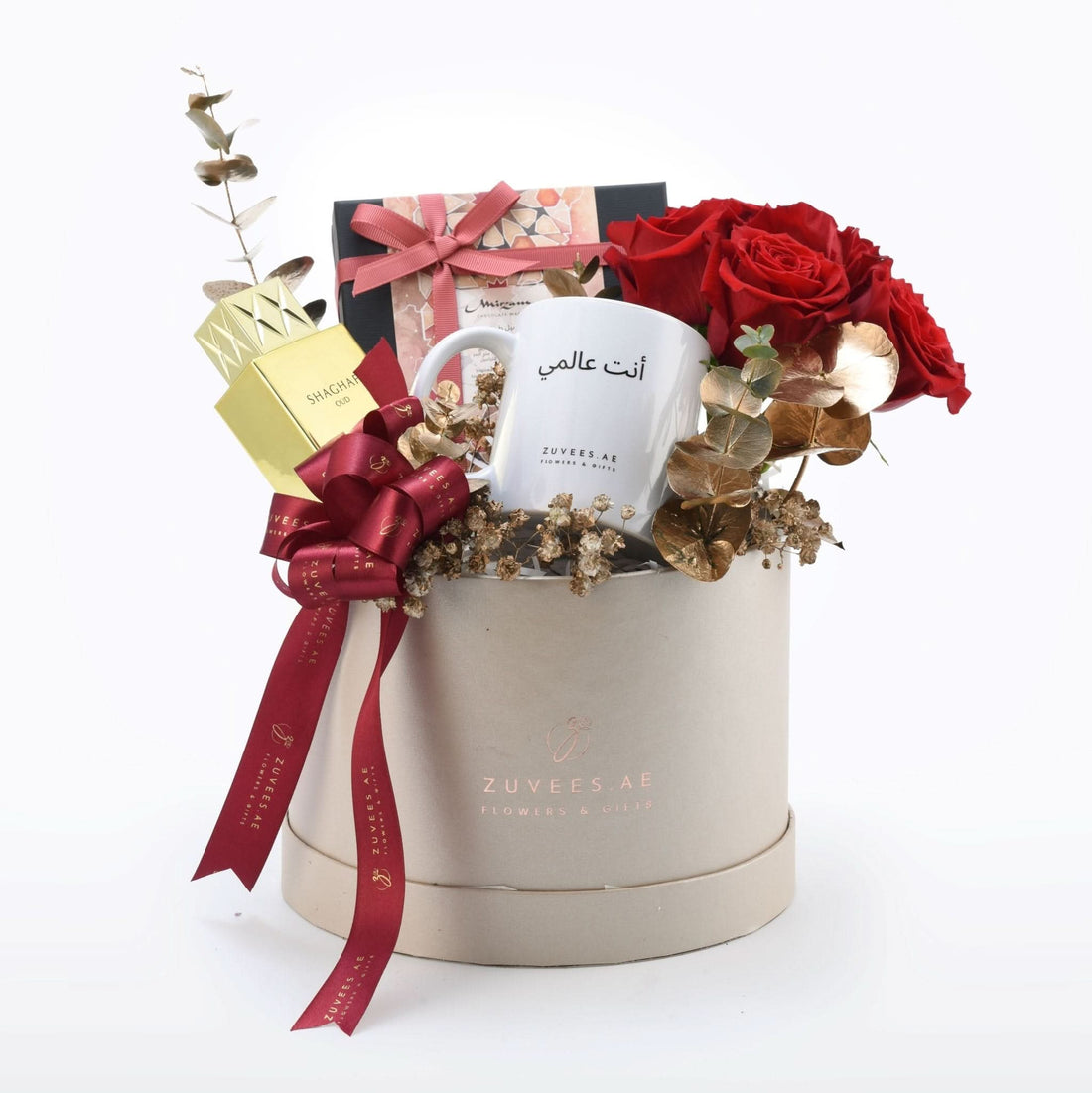 Luxury gift box with red roses, gold eucalyptus, white mug, and perfume, tied with burgundy ribbon.