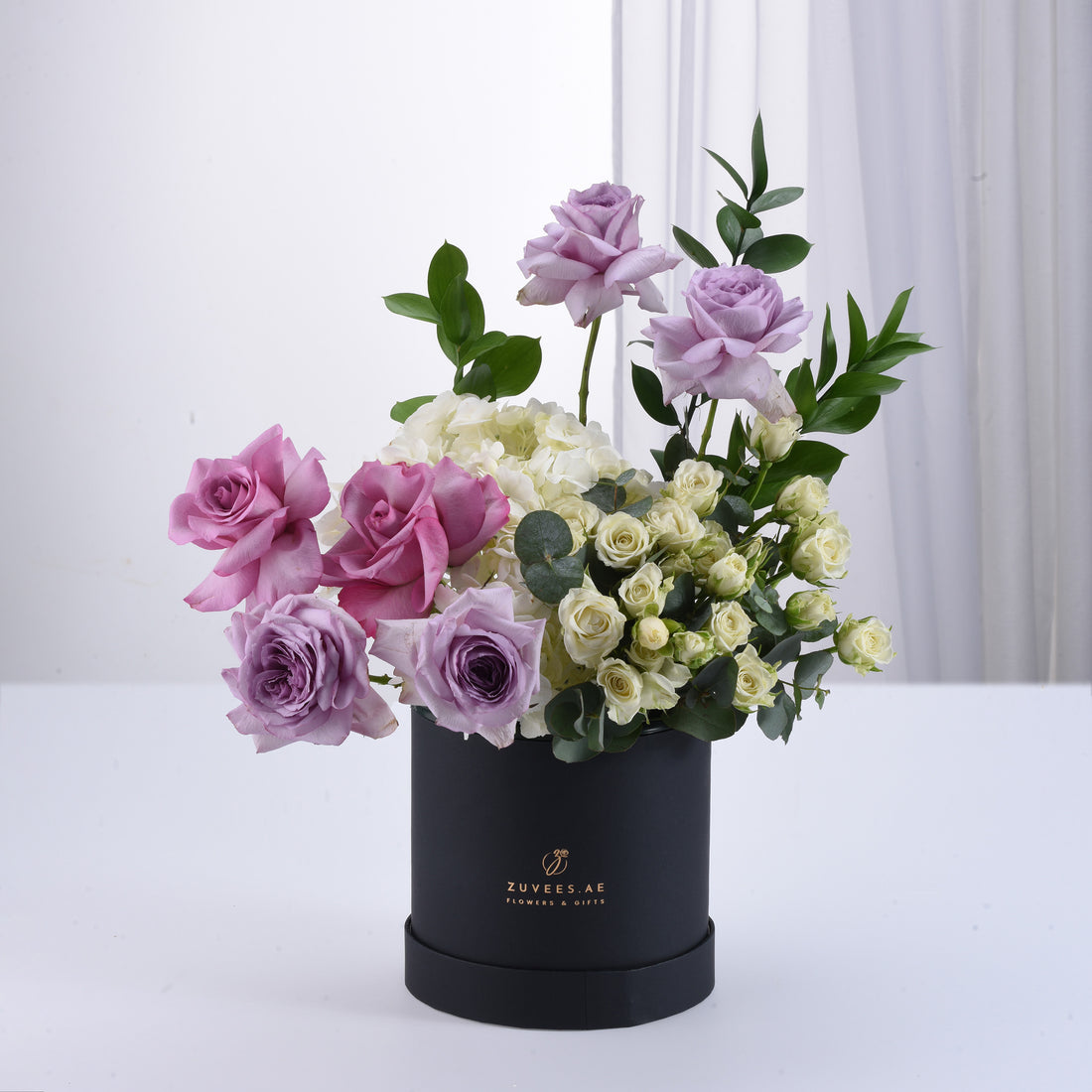 Elegant lavender, pink, and white roses in sleek black box with greenery.