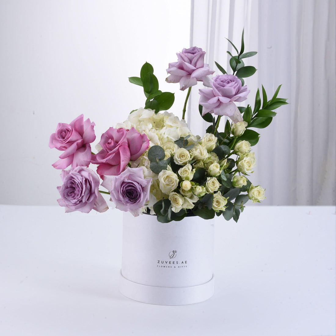 Elegant lavender, pink, and cream roses in white cylindrical box.