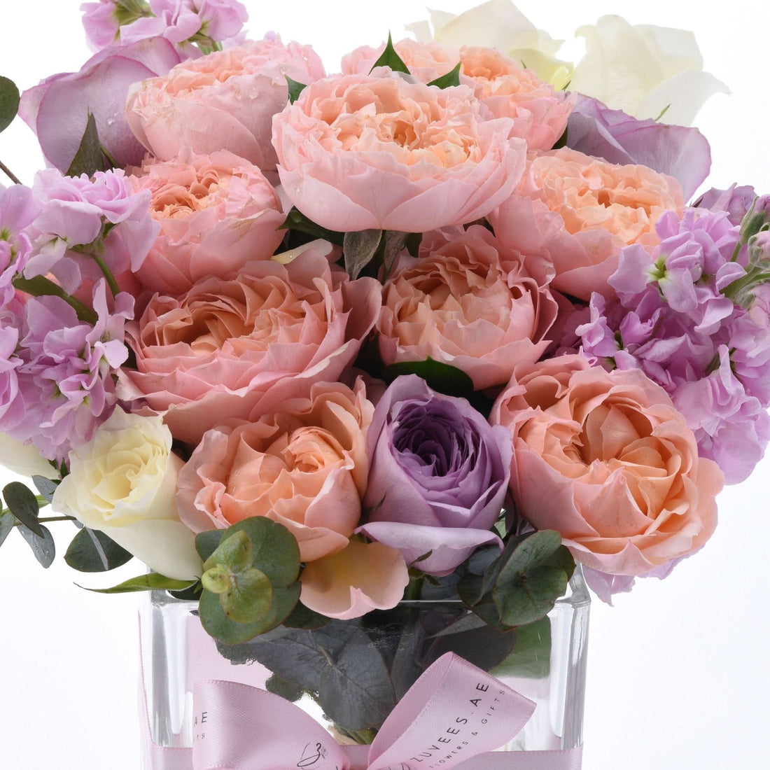 Pastel pink, lavender, and cream roses elegantly arranged in clear glass vase with pink ribbon.
