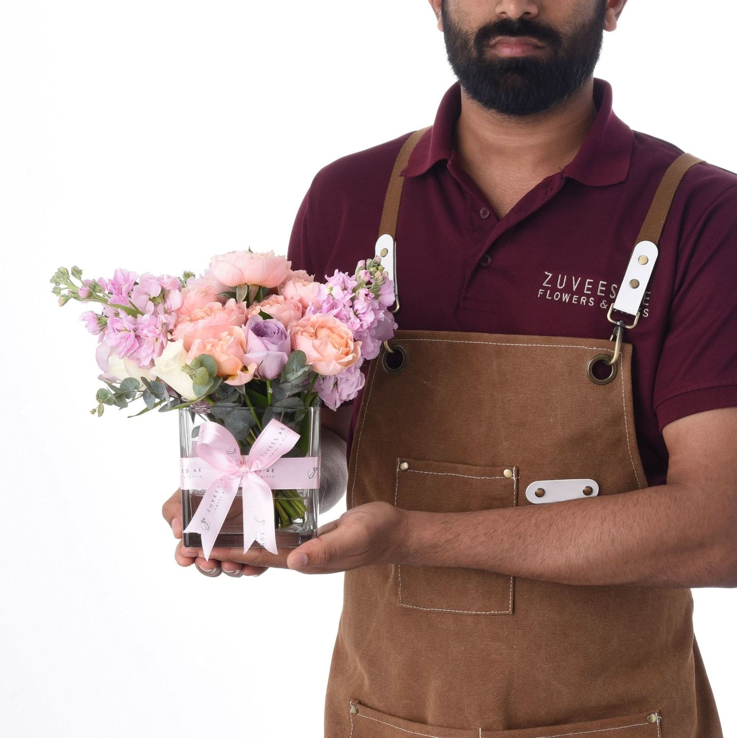 Floral artisan presents pastel bouquet in branded glass vase with pink ribbon.