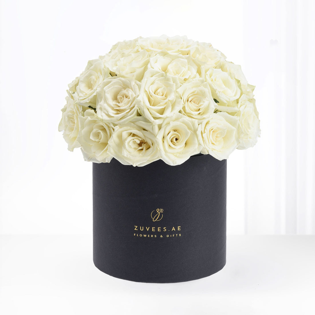 Luxurious cream roses overflowing from a matte black cylindrical box with gold branding.