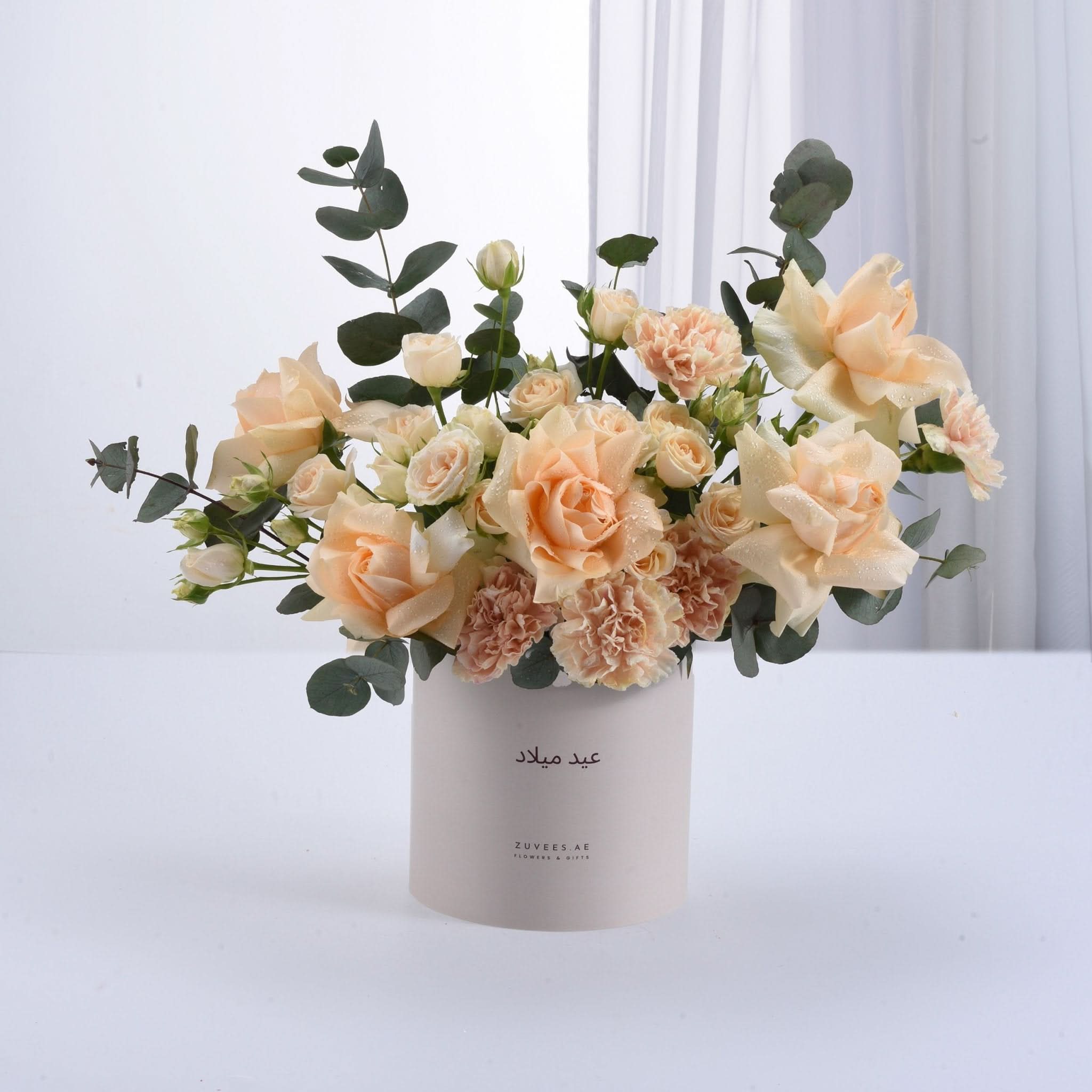 Soft peach roses and carnations in minimalist white cylindrical vase.