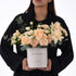 Elegant peach roses, carnations, eucalyptus in white "Happy Birthday" box, held by woman in black.