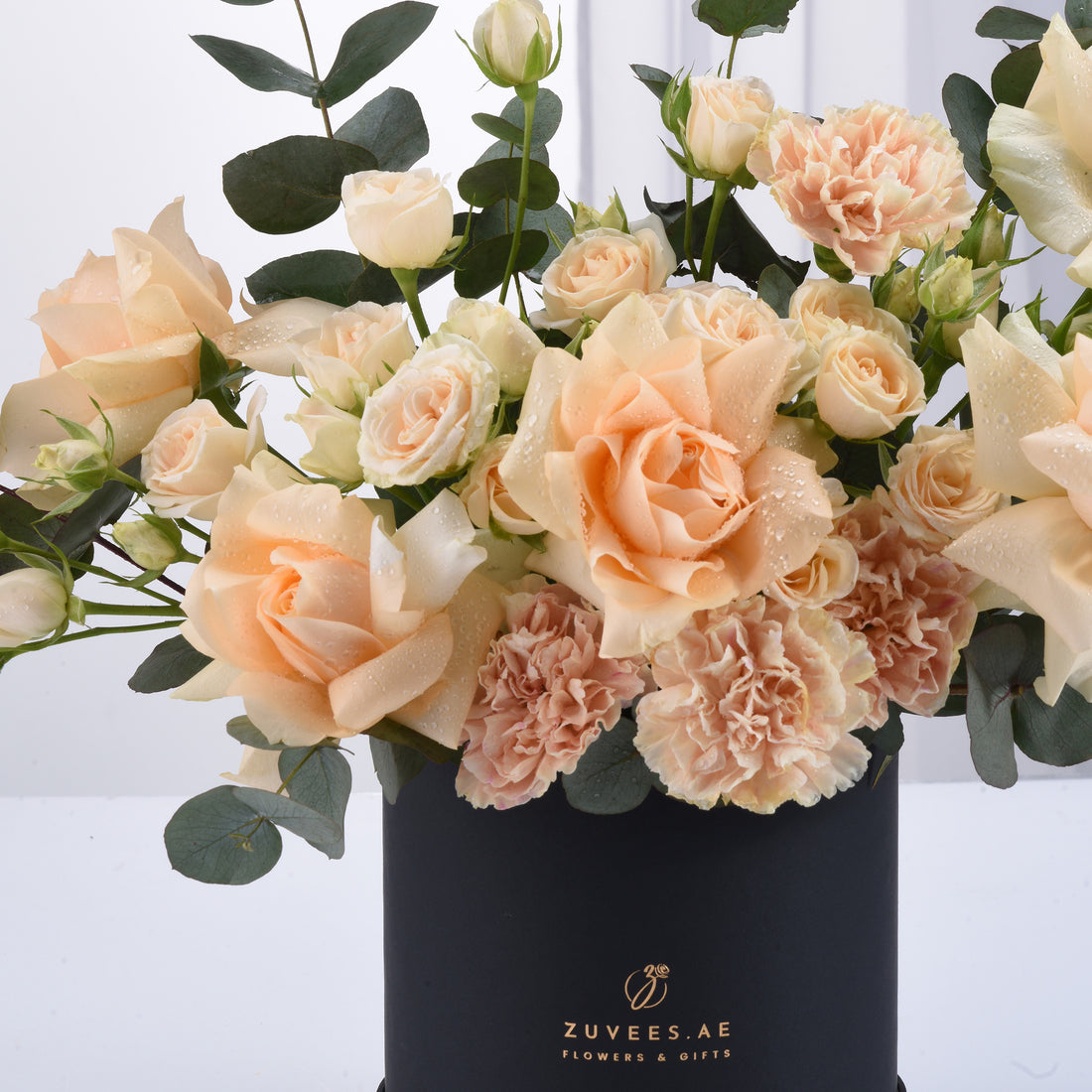 Soft peach roses and carnations in sleek black vase with dew drops.