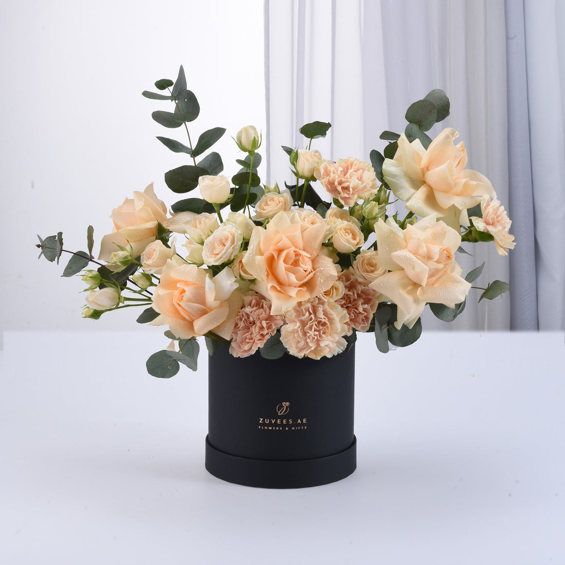 Elegant peach roses and carnations in matte black box with gold logo.