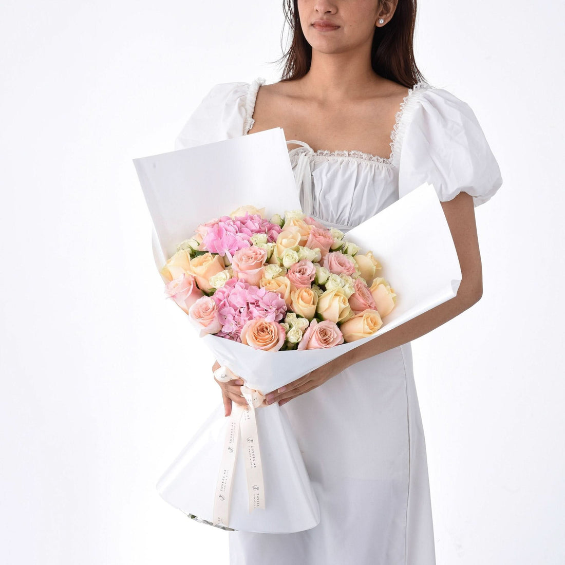 Soft pink and peach roses with hydrangeas, elegantly wrapped in white paper.
