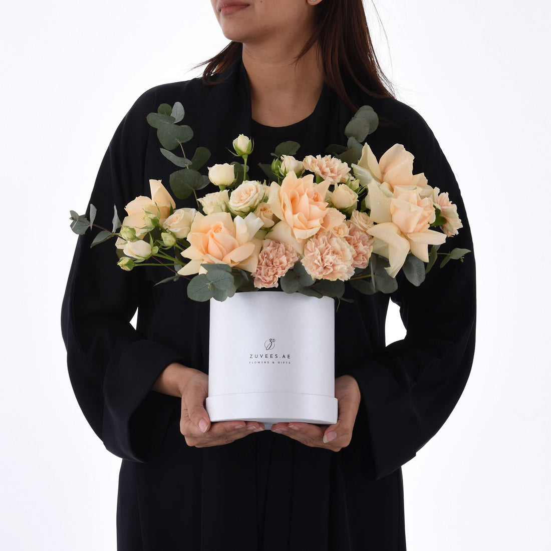 Soft peach roses and carnations in white box held by woman in black.