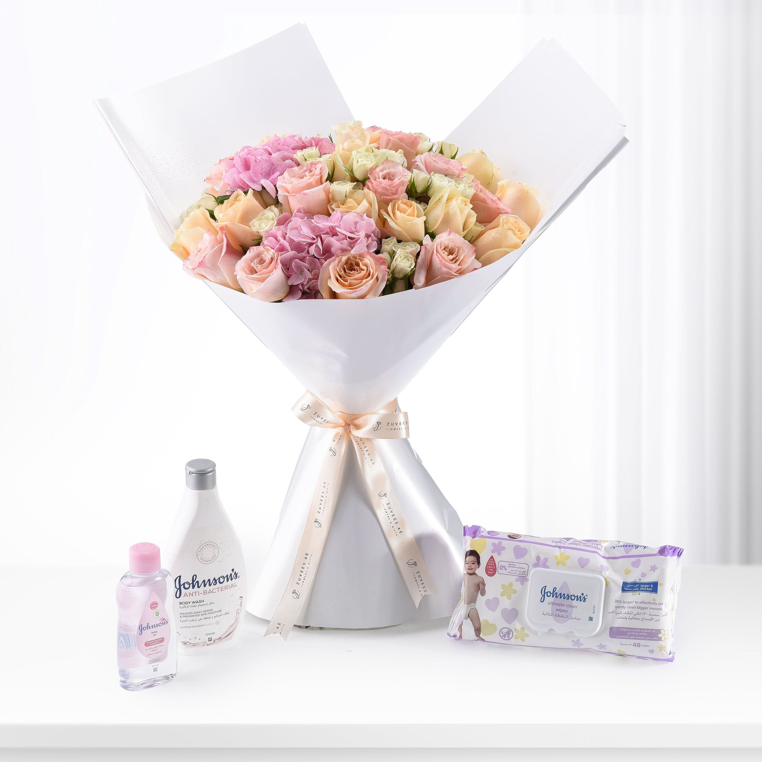 Soft pink roses bouquet with Johnson’s baby care products on white surface.