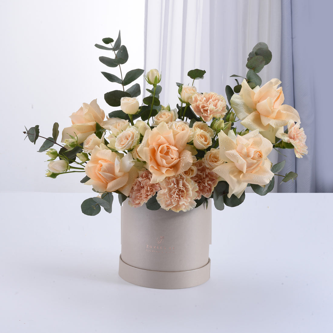 Soft peach roses and carnations in elegant beige hat box with eucalyptus.