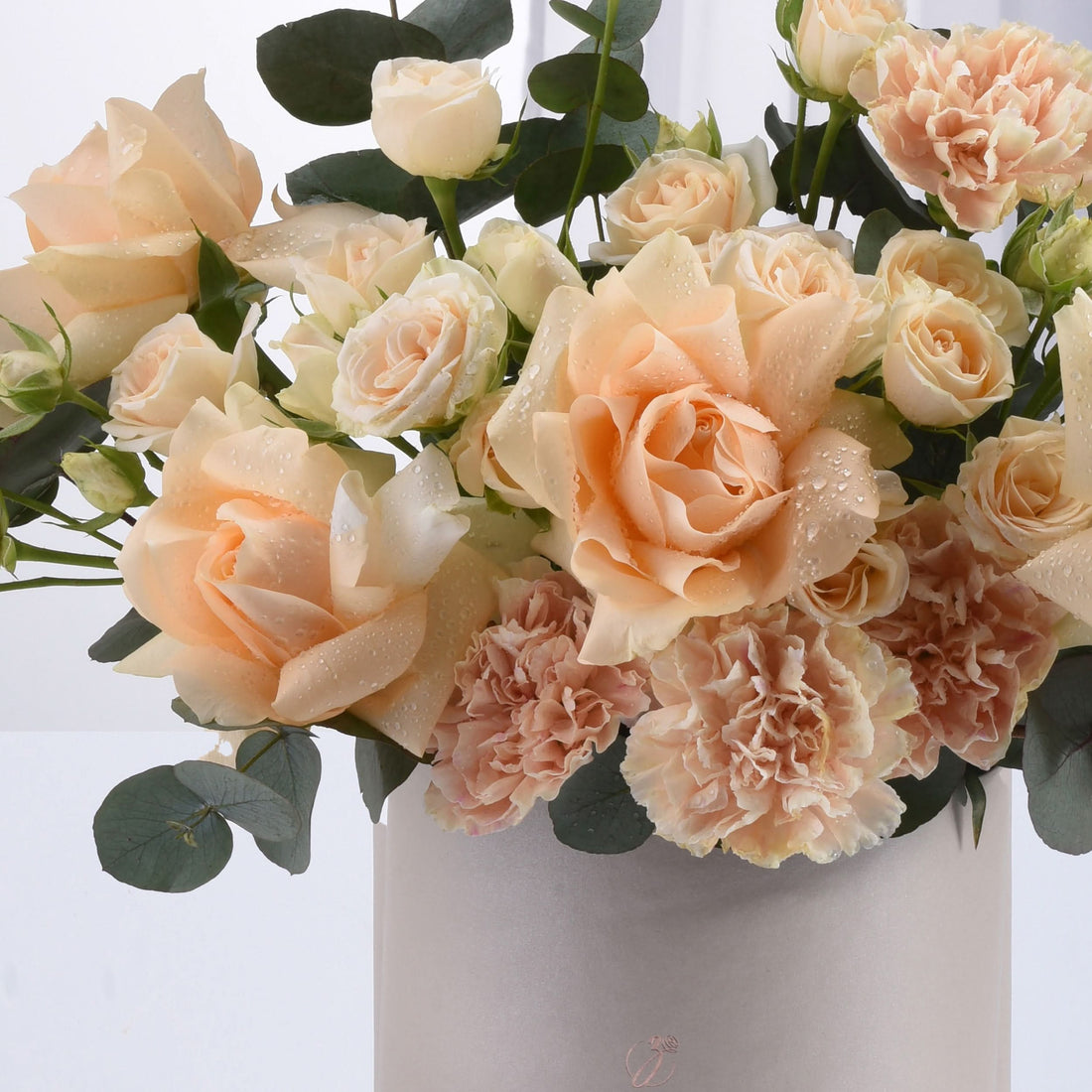 Soft peach roses and carnations glisten with dewdrops in minimalist vase.