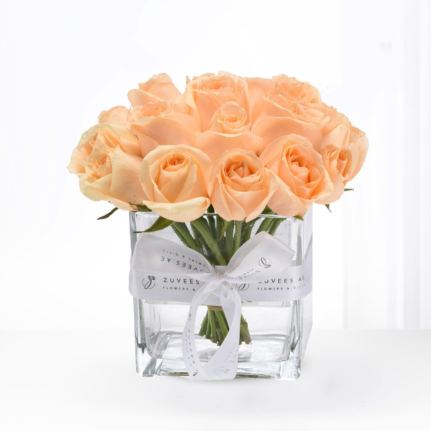 Soft peach roses in clear glass vase, elegantly tied with branded white ribbon.