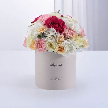 Pastel-hued floral arrangement in beige box with Arabic greeting.