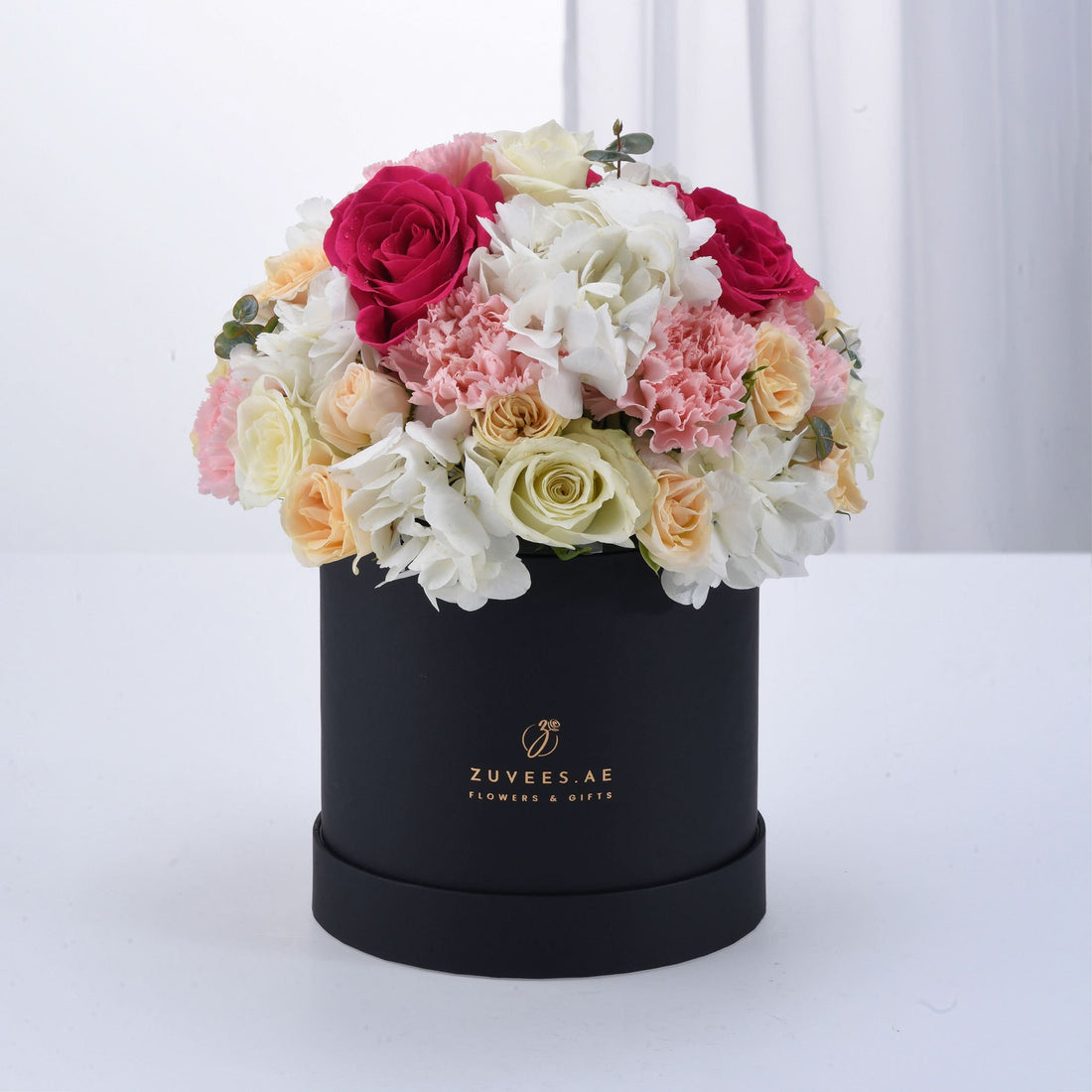 Elegant black hat box overflowing with vibrant pink, white, and peach roses and hydrangeas.
