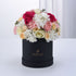Elegant black hat box overflowing with vibrant pink, white, and peach roses and hydrangeas.