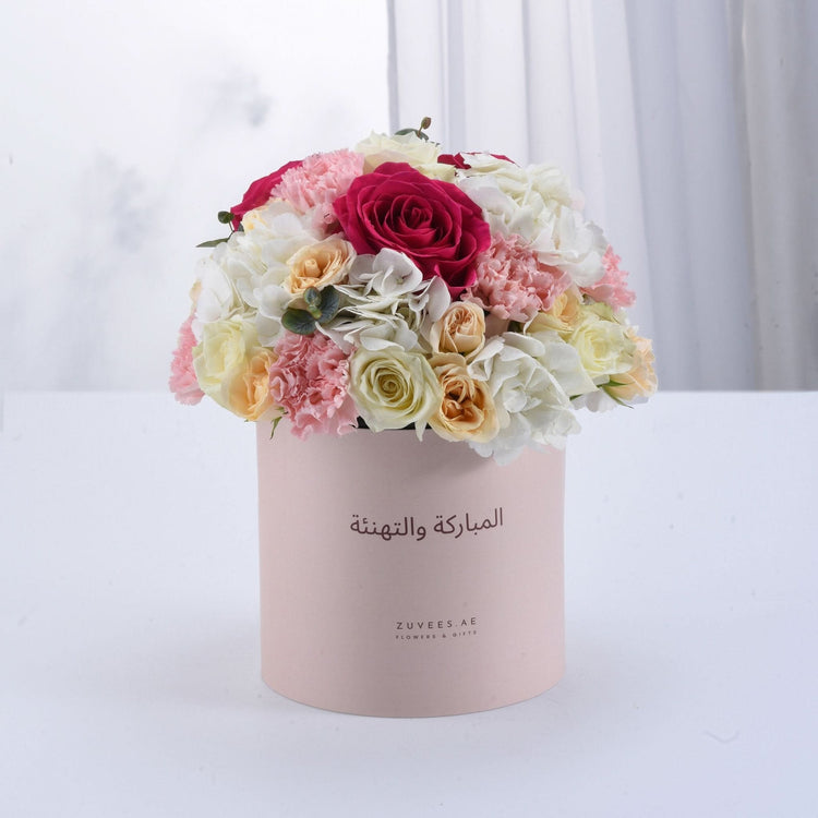 Soft pink box holds vibrant roses, hydrangeas, and carnations for elegant celebration.