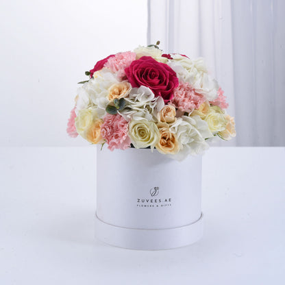 White box overflowing with vibrant pink, cream, and red roses, carnations, and hydrangeas.