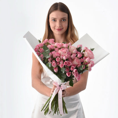 Woman holds lush pink rose bouquet wrapped in white paper with pink ribbon.