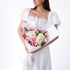 Elegant woman in white dress holds bouquet of pink roses and white hydrangeas, wrapped in white paper with pink ribbon.
