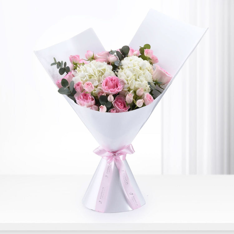 Soft pink roses and white hydrangeas elegantly wrapped in white paper with a pink ribbon.