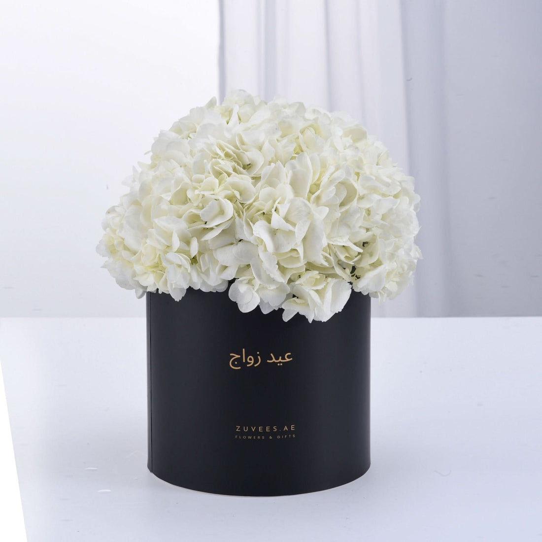 Elegant white hydrangeas in matte black box with gold Arabic script.