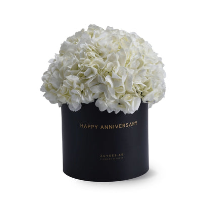 Elegant white hydrangeas in black "Happy Anniversary" gift box, gold lettering, minimalist luxury floral arrangement.