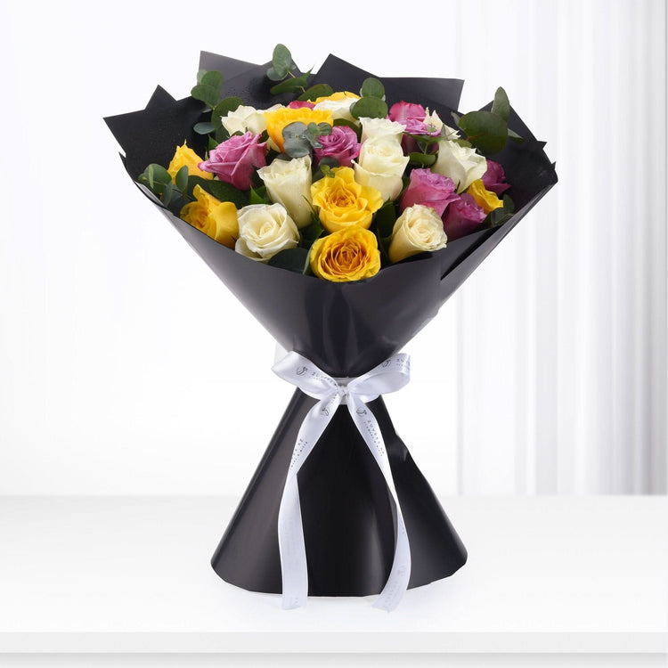 Vibrant yellow, pink, and white roses wrapped in sleek black paper with elegant white ribbon.
