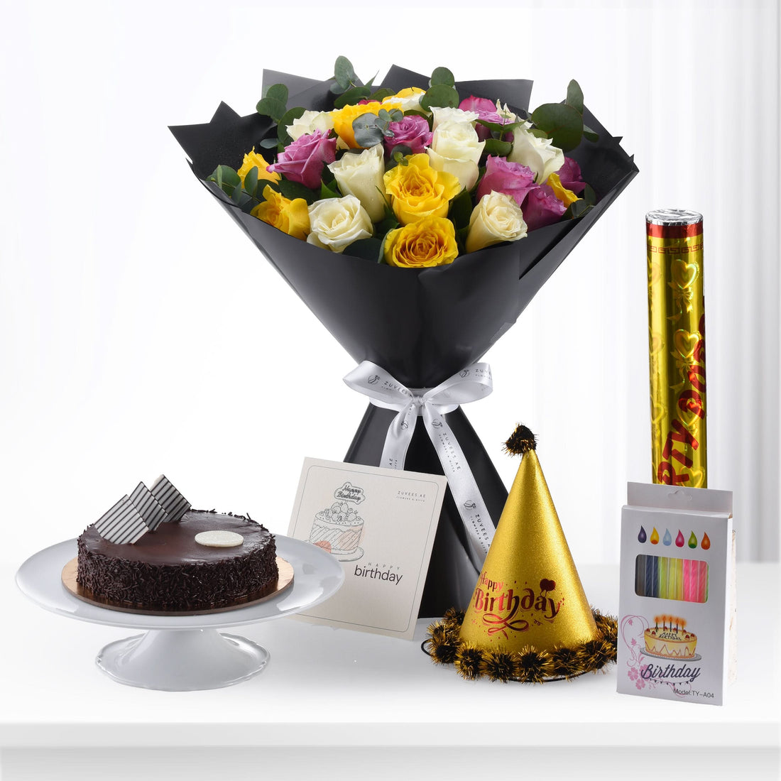 Vibrant multi-colored roses, chocolate cake, and festive birthday accessories arranged elegantly.