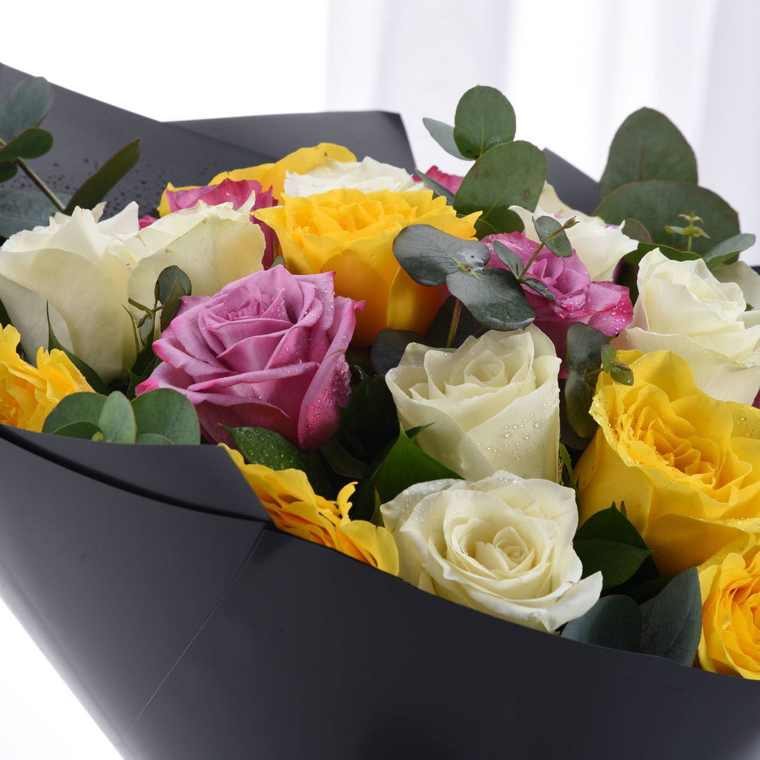 Vibrant yellow, pink, and white roses with eucalyptus, dew drops, black wrapping.