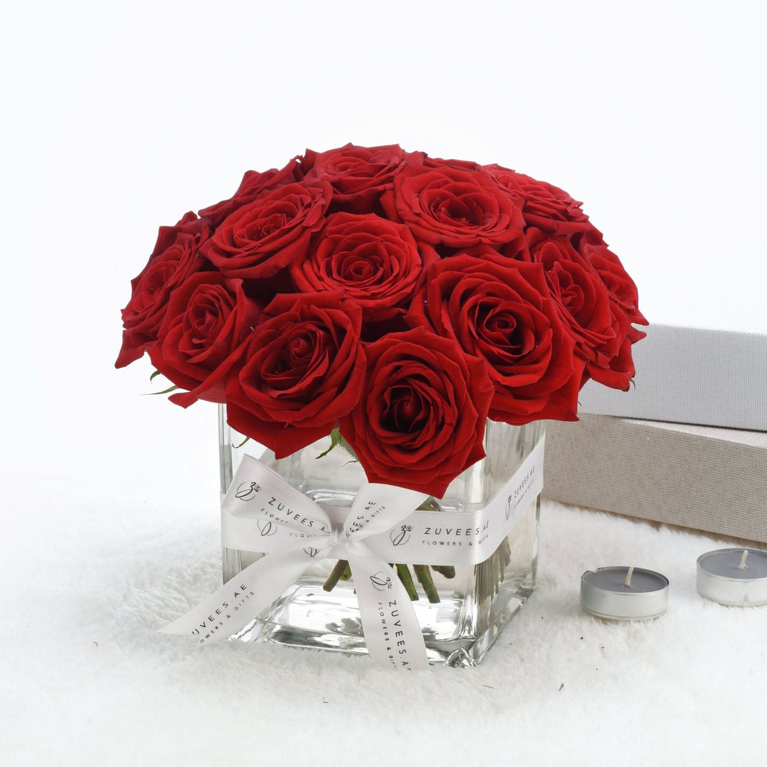 Vibrant red roses in clear glass vase, elegantly tied with branded white ribbon.
