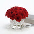 Vibrant red roses in clear glass vase, elegantly tied with branded white ribbon.