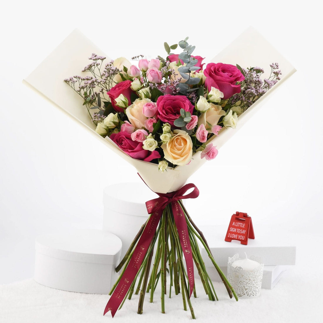 Vibrant pink, peach, and white roses wrapped in cream paper with burgundy ribbon.