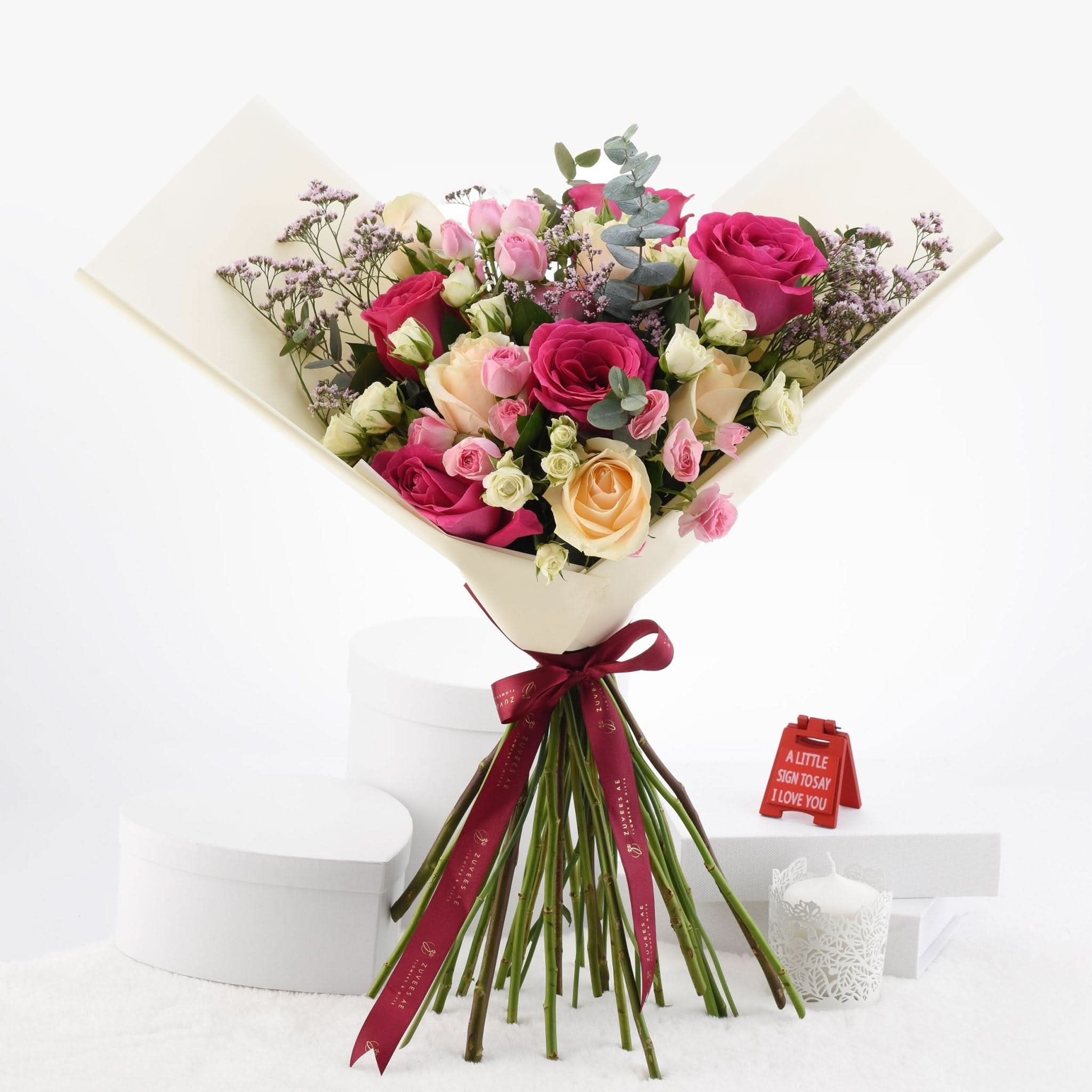 Vibrant pink, peach, and white roses wrapped in cream paper with burgundy ribbon.