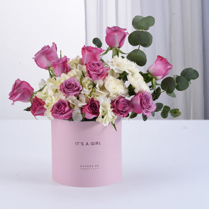 Pink box holds vibrant roses and hydrangeas, celebrating “It’s a Girl” with elegant greenery.