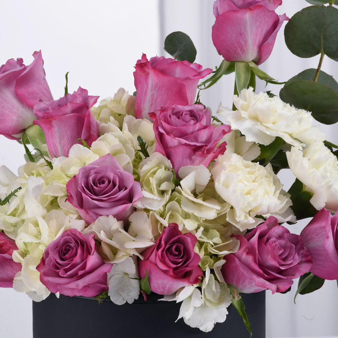 Vibrant pink roses, white hydrangeas, and eucalyptus in sleek black vase.