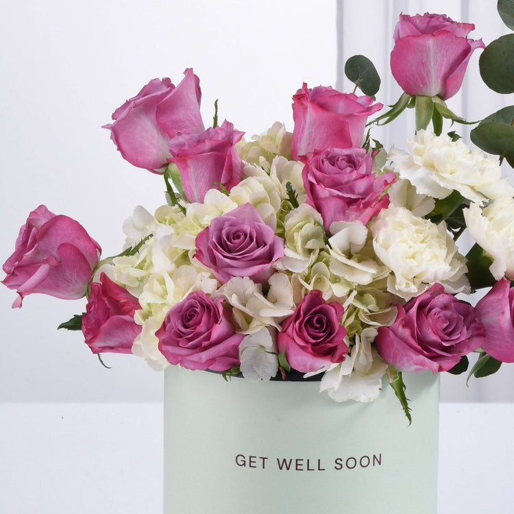 Pastel mint box holds vibrant pink roses and white hydrangeas, "Get Well Soon" message.