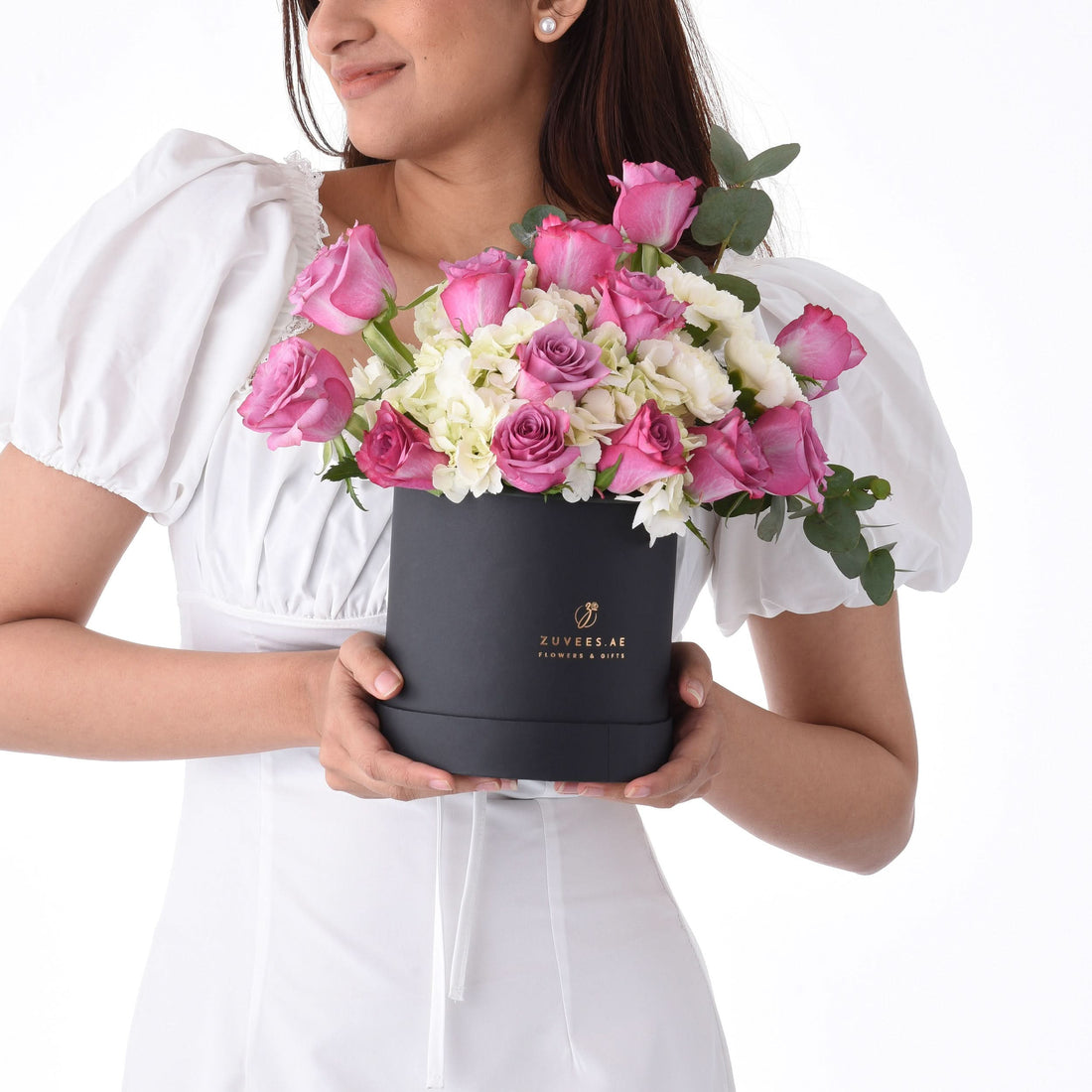 Elegant woman holds black box filled with pink roses and white hydrangeas.