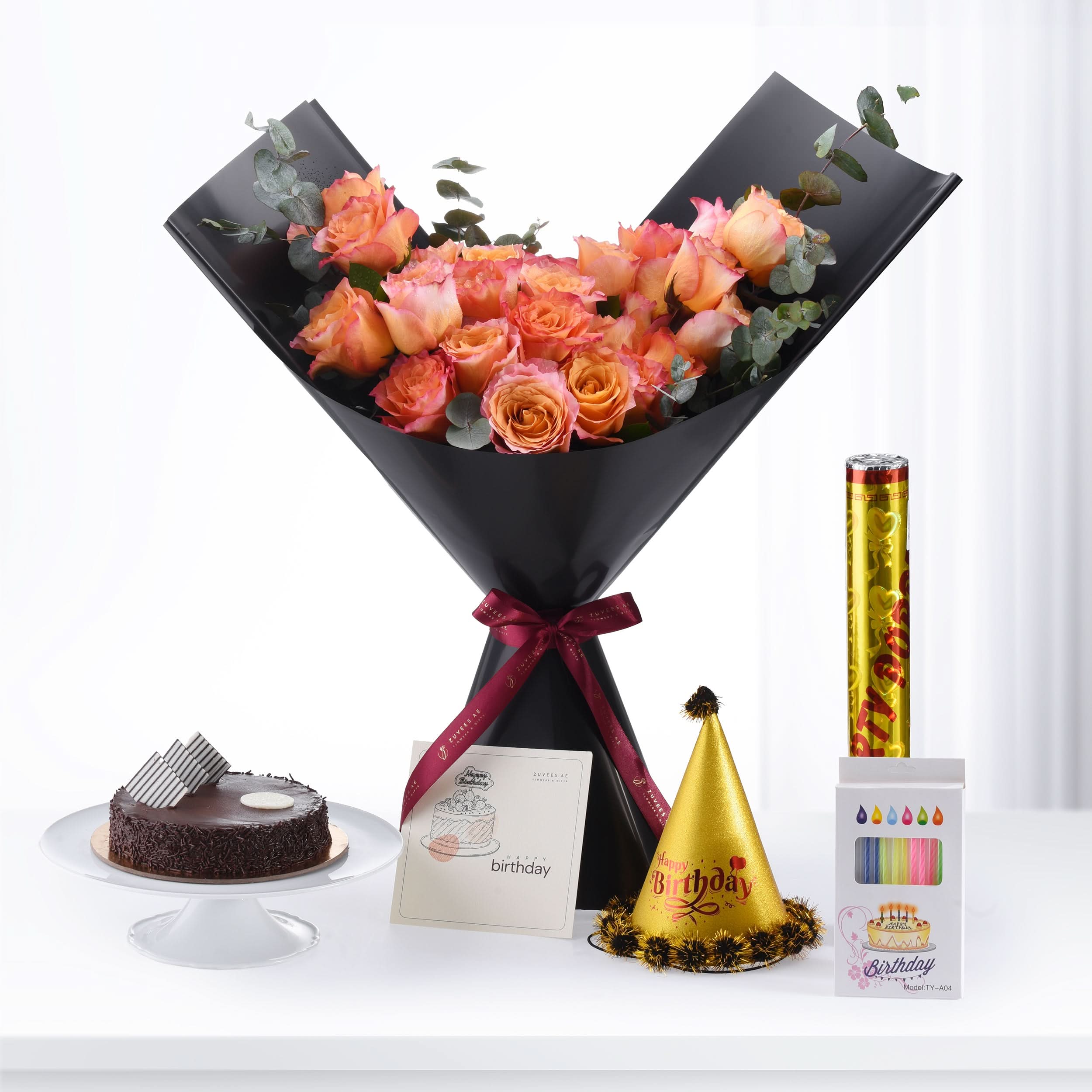 Black-wrapped peach roses, chocolate cake, party hat, and candles for birthday celebration.