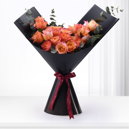 Vibrant orange-pink roses with eucalyptus, elegantly wrapped in black paper, tied with burgundy ribbon.