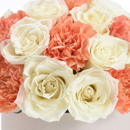 Cream roses and coral carnations in soft, elegant arrangement.