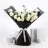Elegant white roses in sleek black wrap, accented with silver ribbon and eucalyptus, set against minimalist white backdrop.