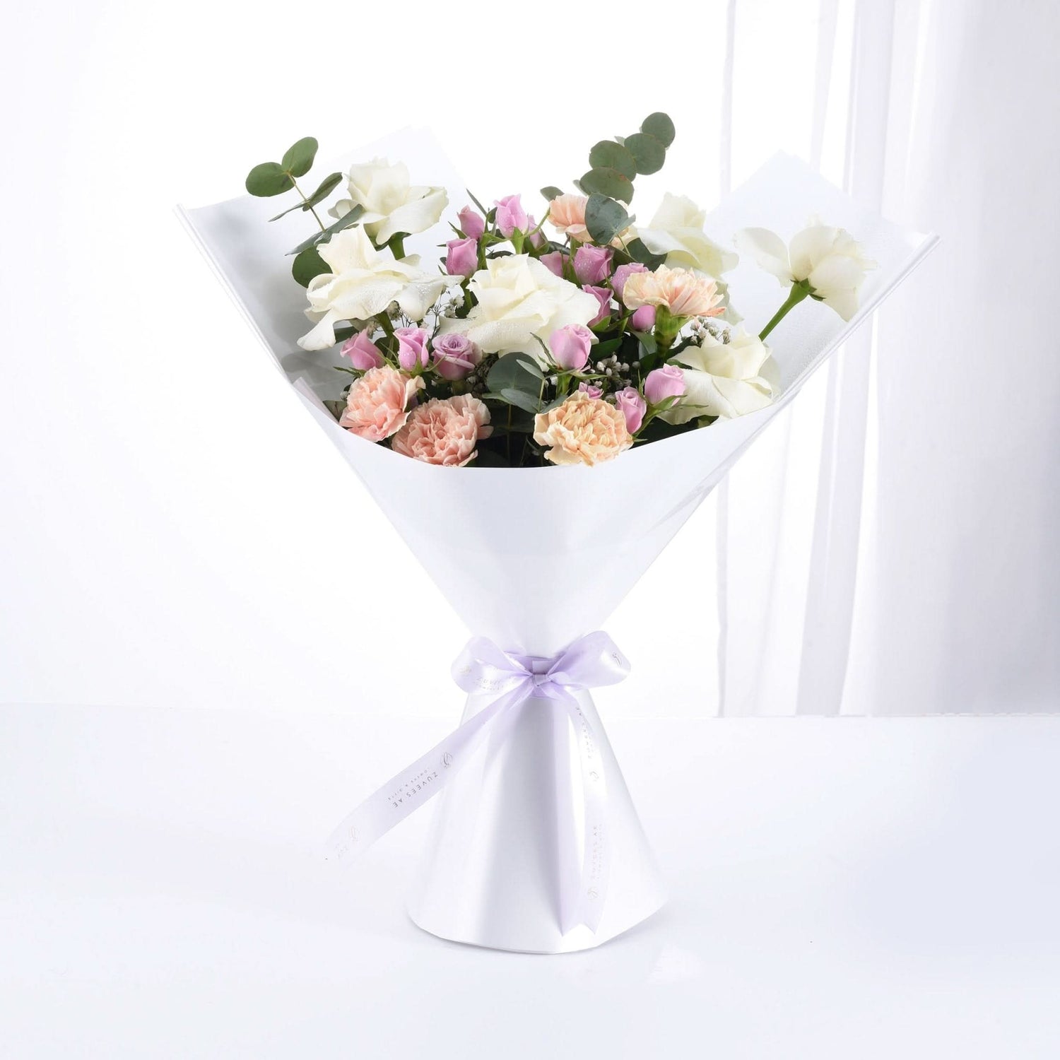 Soft pastel roses and eucalyptus wrapped in white paper with lavender ribbon.