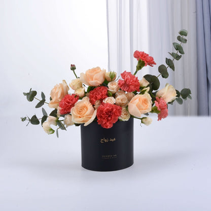 Elegant peach roses, coral carnations, and eucalyptus in a sleek black gift box.