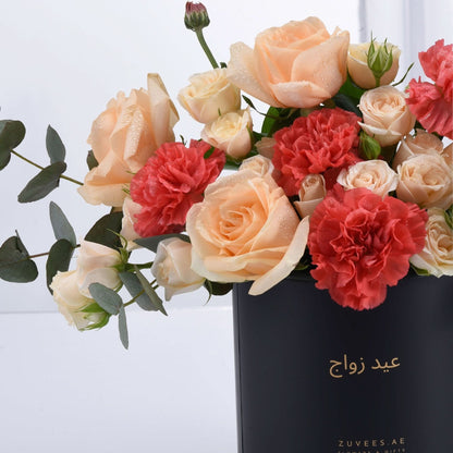 Elegant peach roses and coral carnations in sleek black vase with gold text.