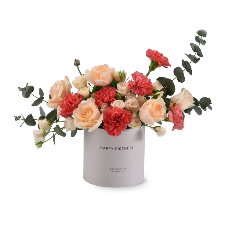 Pastel peach roses and coral carnations in sleek gray "Happy Birthday" box.